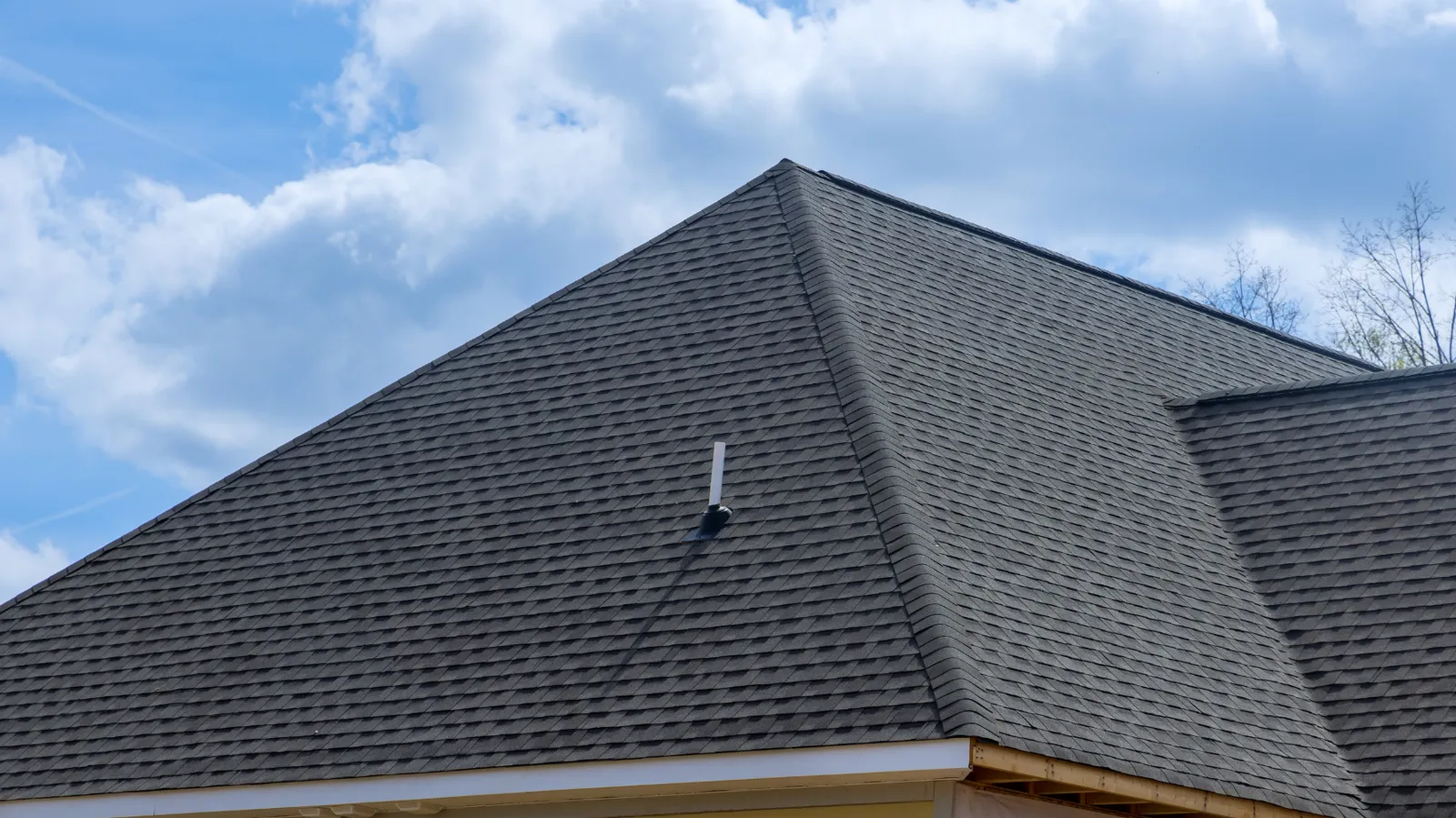 Cloudy sky over a dark shingle hip roof with vent pipe