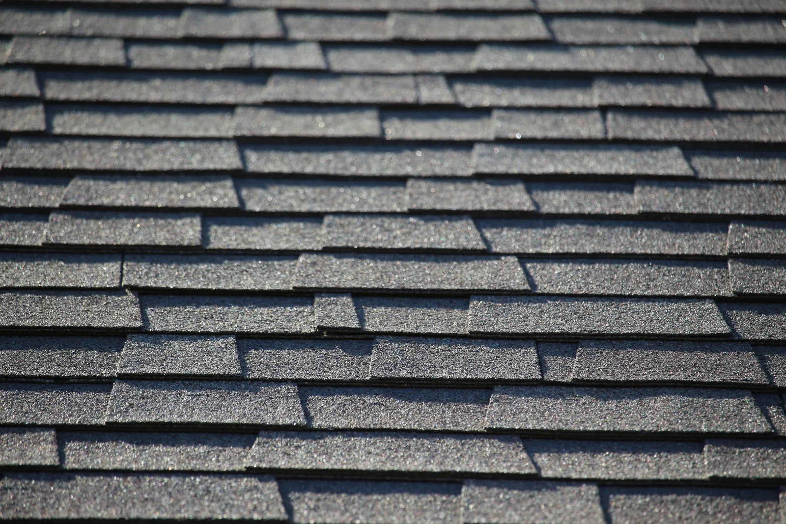 Sunlit dark asphalt shingle courses casting strong shadows