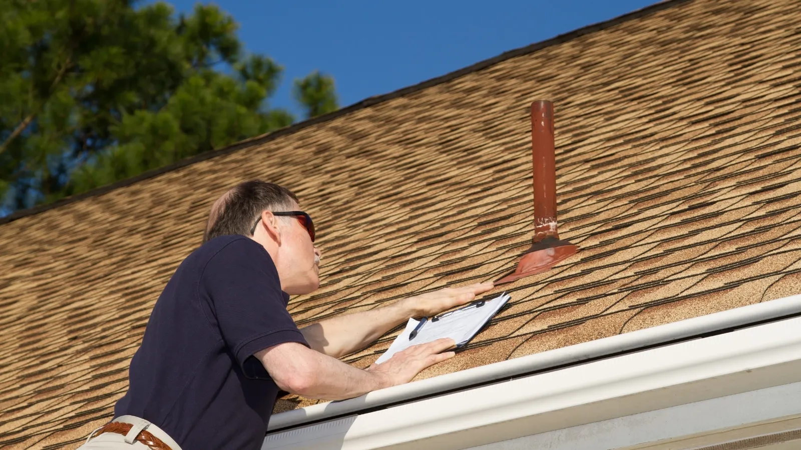 With a clipboard an inspector checks shingles around a vent pipe