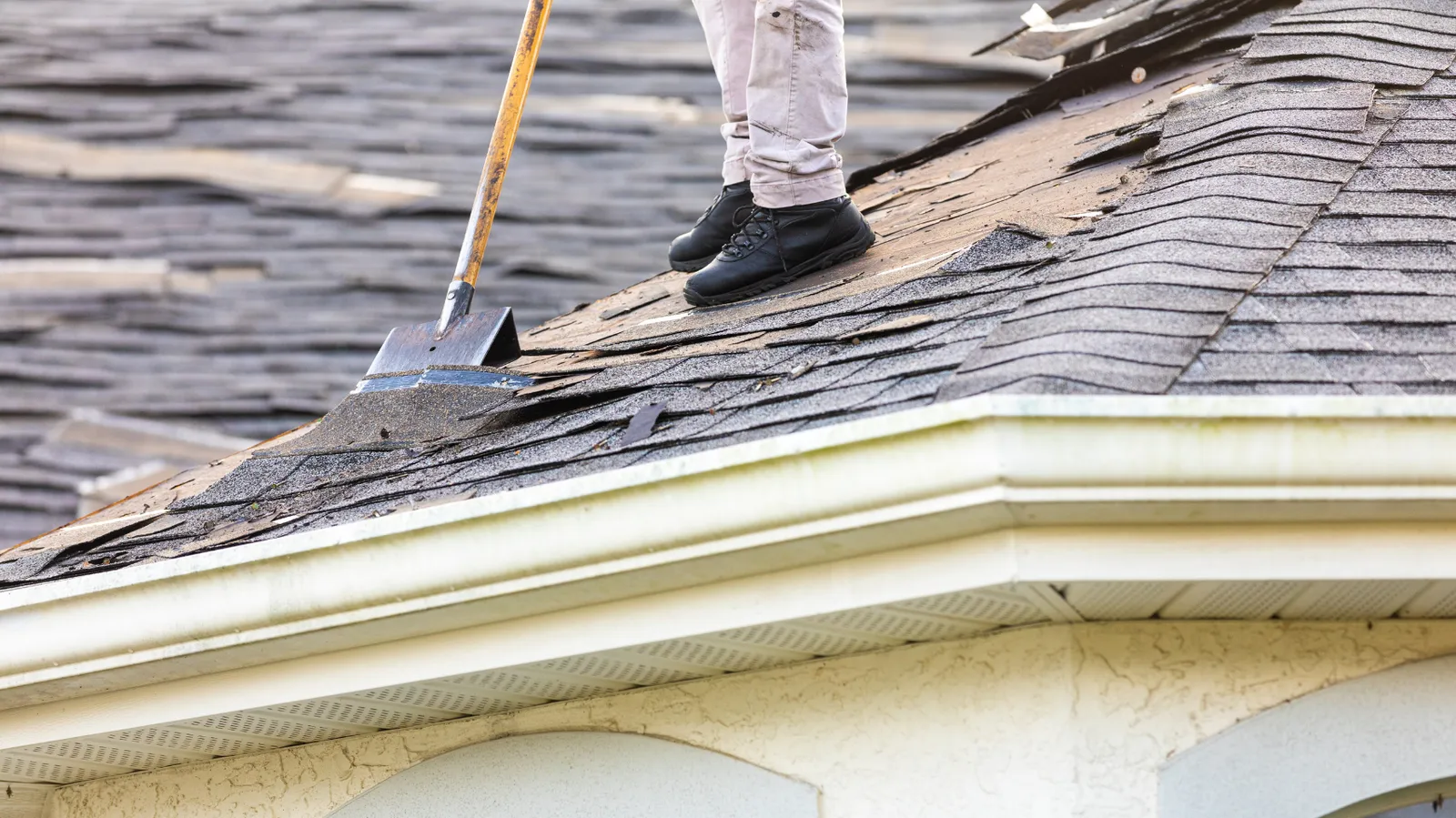 At a roof edge stands a roofer with a shovel wedged under shingles